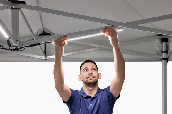 The man attaches the LED strips to the folding gazebo.